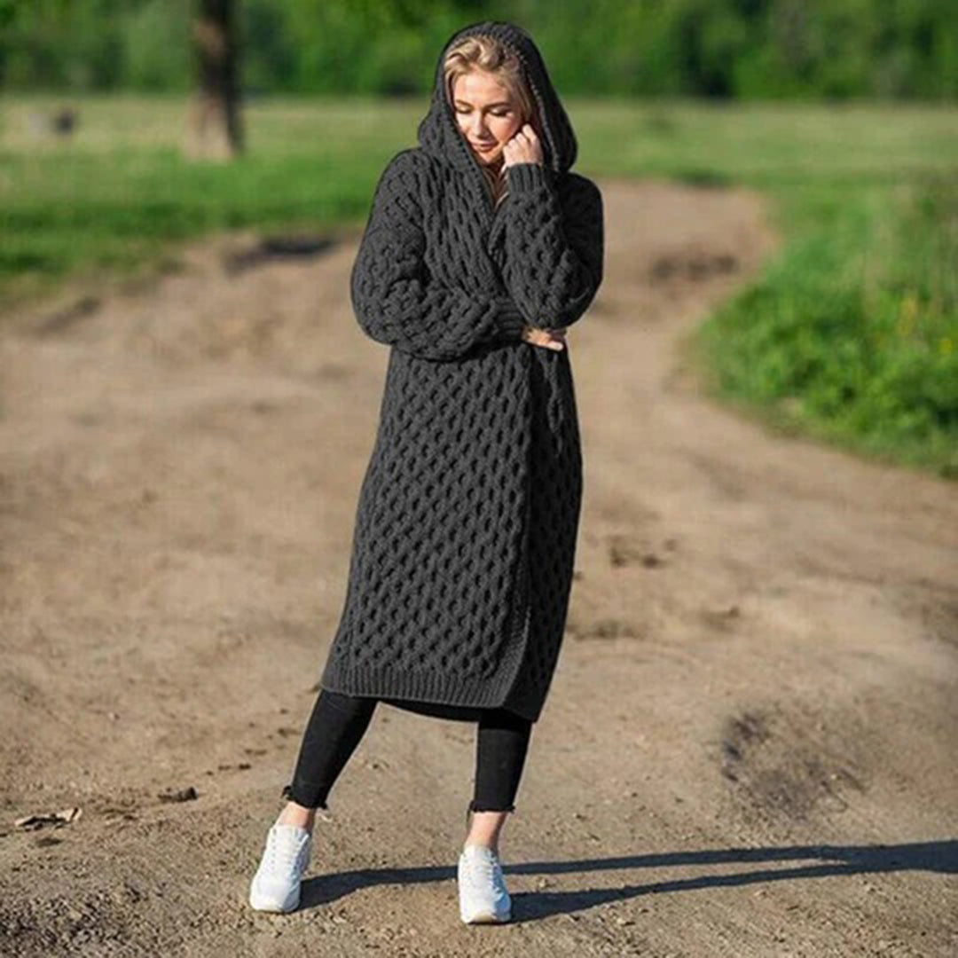 Donna con cappotto lungo a maglia grigio scuro, cappuccio, su strada sterrata. Moda autunnale, abbigliamento casual, stile confortevole.
