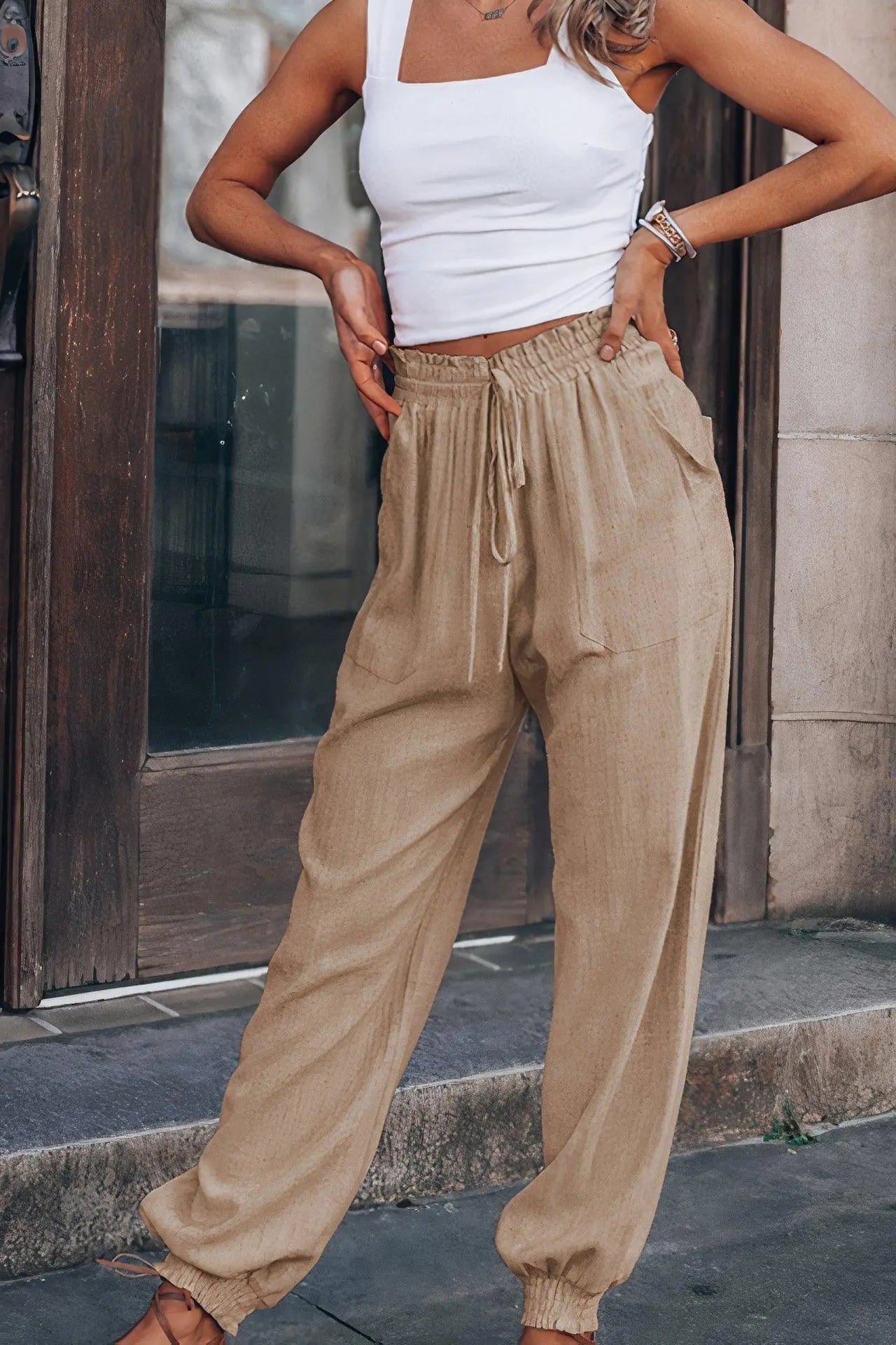 Pantaloni larghi beige da donna, stile casual, con elastico in vita e tasche, abbinati a top bianco. Look estivo alla moda per passeggiate urbane.