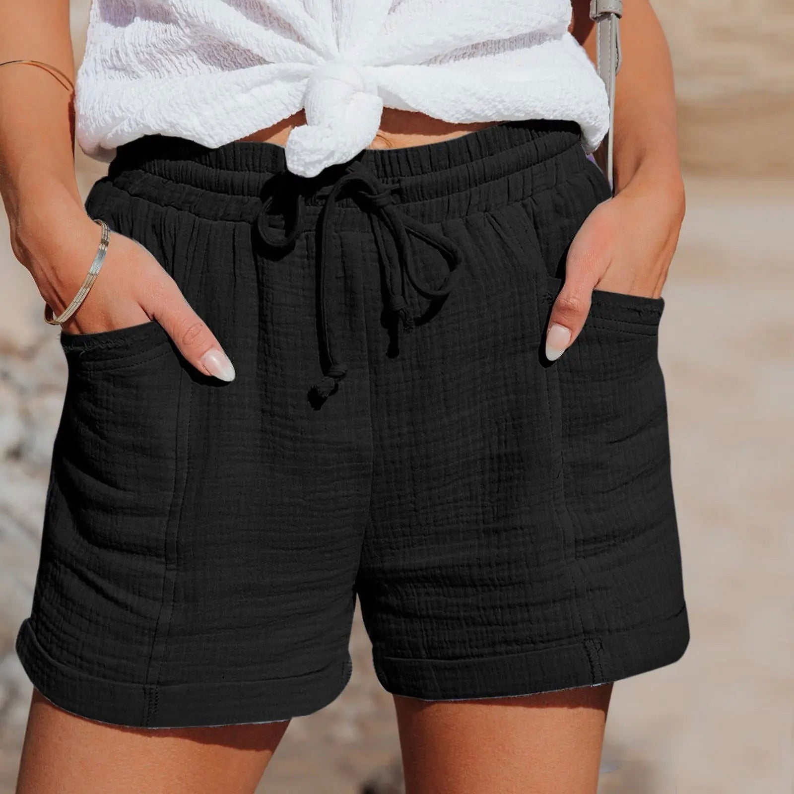 Shorts neri da donna in cotone, con tasche e laccio in vita, indossati con top bianco annodato. Stile casual estivo, moda femminile.