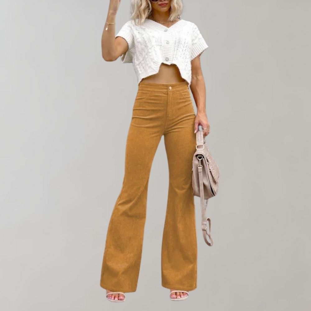 Donna con pantaloni a zampa color senape e top bianco corto, borsa a tracolla beige, sfondo grigio. Moda casual, abbigliamento femminile trendy.