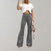 Donna con pantaloni a zampa grigi e top bianco corto, borsa beige, sfondo neutro. Moda casual, abbigliamento femminile trendy.