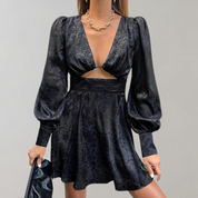 Abito nero elegante con maniche a sbuffo e scollatura profonda, dettagli in pizzo, indossato da donna con collana dorata. Moda femminile chic.
