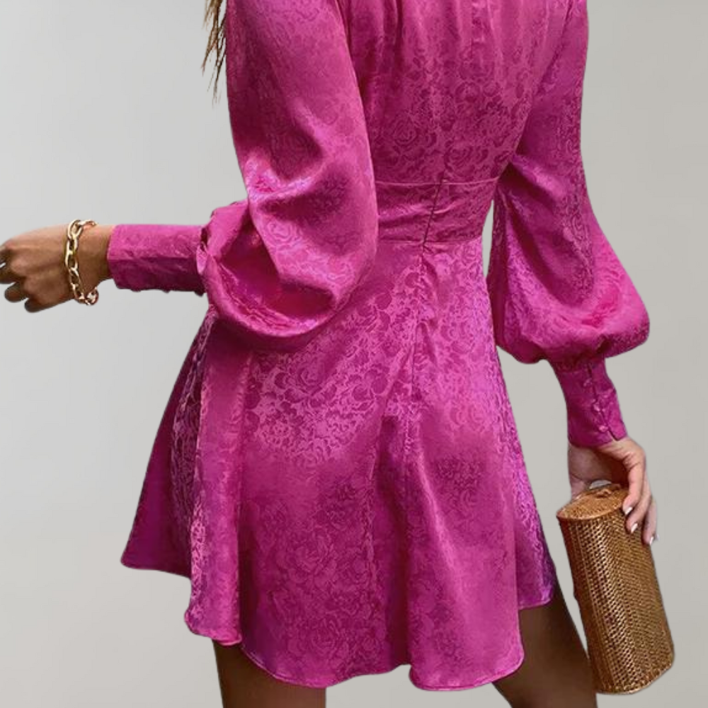 Vestito corto fucsia in raso con maniche lunghe a sbuffo, motivo floreale, abbinato a pochette dorata. Elegante abbigliamento femminile da sera.