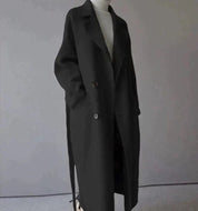 Cappotto nero lungo elegante, doppio petto, con cintura, indossato su maglione bianco. Moda autunnale, abbigliamento donna, stile minimalista.