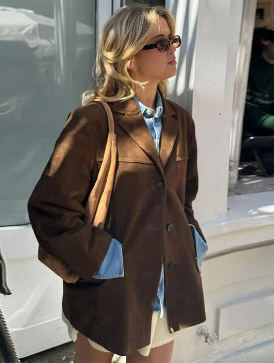 Donna con occhiali da sole indossa giacca marrone oversize e camicia di jeans, moda autunnale casual, stile urbano, strada cittadina.