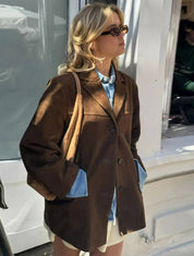 Donna con occhiali da sole indossa giacca marrone oversize e camicia di jeans, moda autunnale casual, stile urbano, strada cittadina.