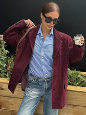 Donna con occhiali da sole indossa giacca bordeaux su camicia azzurra e jeans, tiene caffè in mano. Moda autunnale casual chic.