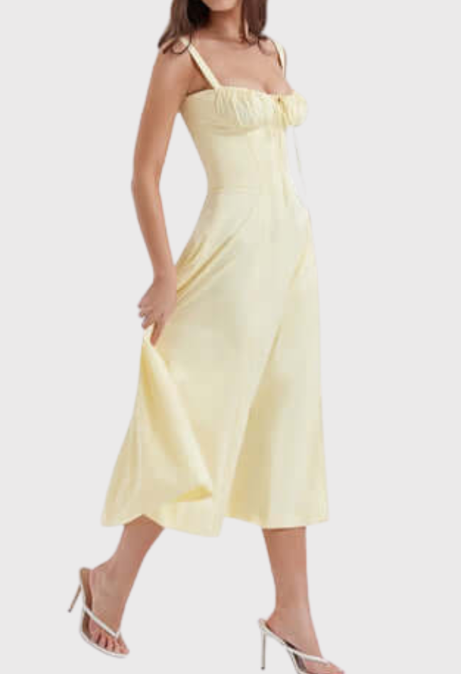 Abito midi giallo chiaro estivo da donna, con spalline sottili e scollo a cuore, abbinato a sandali bianchi con tacco.
