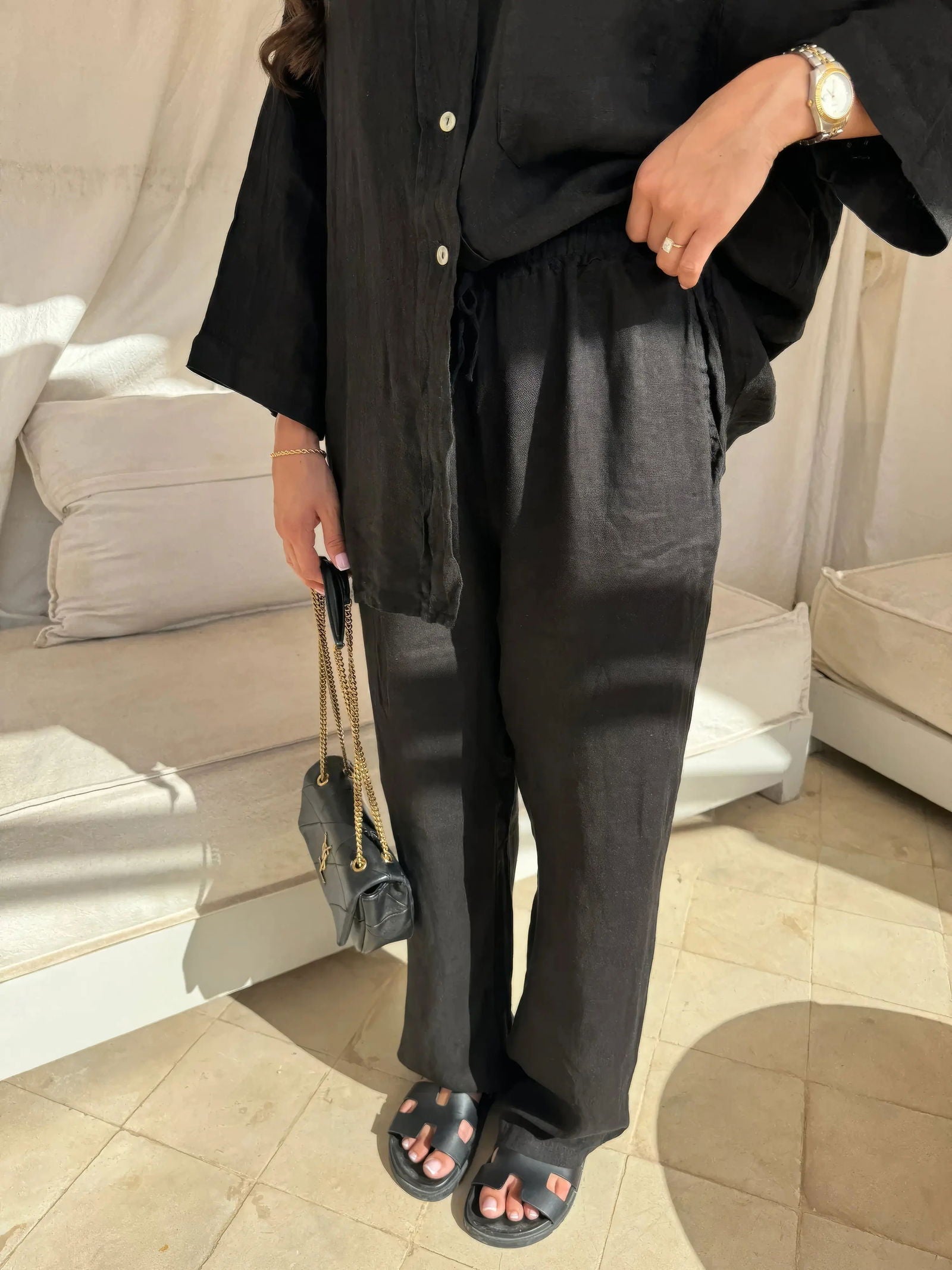 Donna in abbigliamento nero casual, con camicia e pantaloni larghi, sandali neri e borsa a tracolla. Stile minimalista ed elegante.