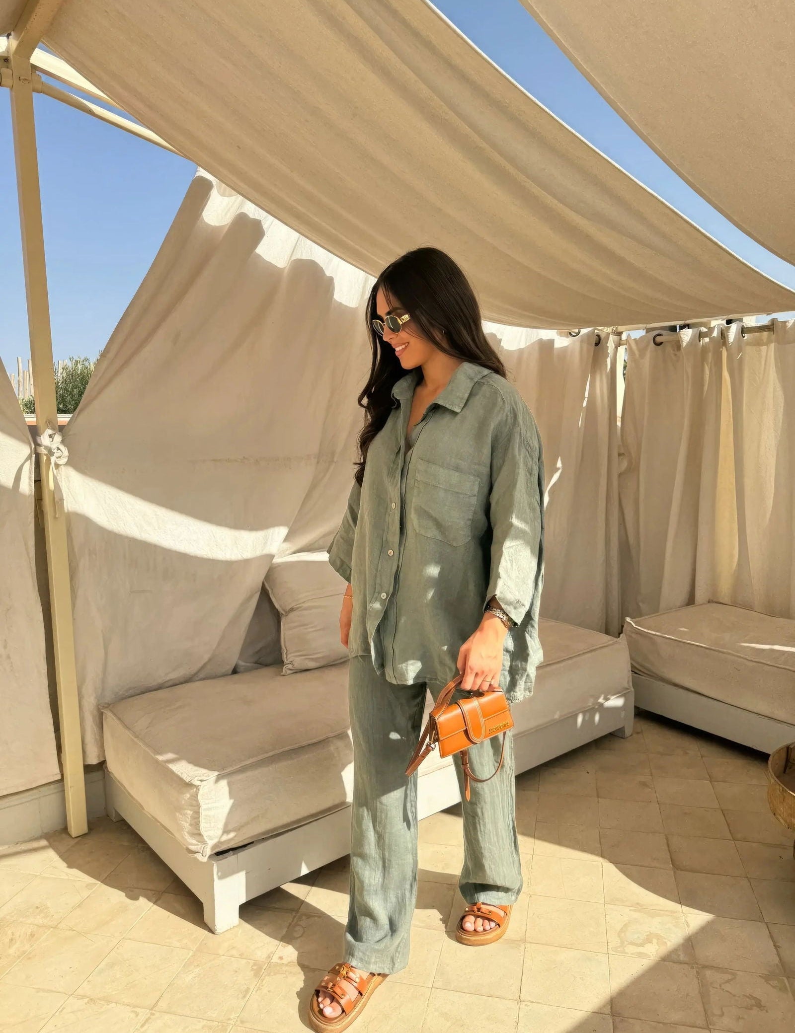 Donna con abito coordinato verde, occhiali da sole e borsa arancione in un'area lounge all'aperto. Moda estiva, stile casual chic.