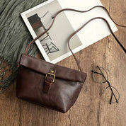 Borsa a tracolla in pelle marrone su tavolo di legno, accanto a occhiali e rivista. Elegante accessorio moda donna, stile vintage.