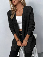 Donna con cardigan nero lavorato a maglia, top bianco e jeans neri. Moda autunnale, abbigliamento casual elegante, stile femminile moderno.