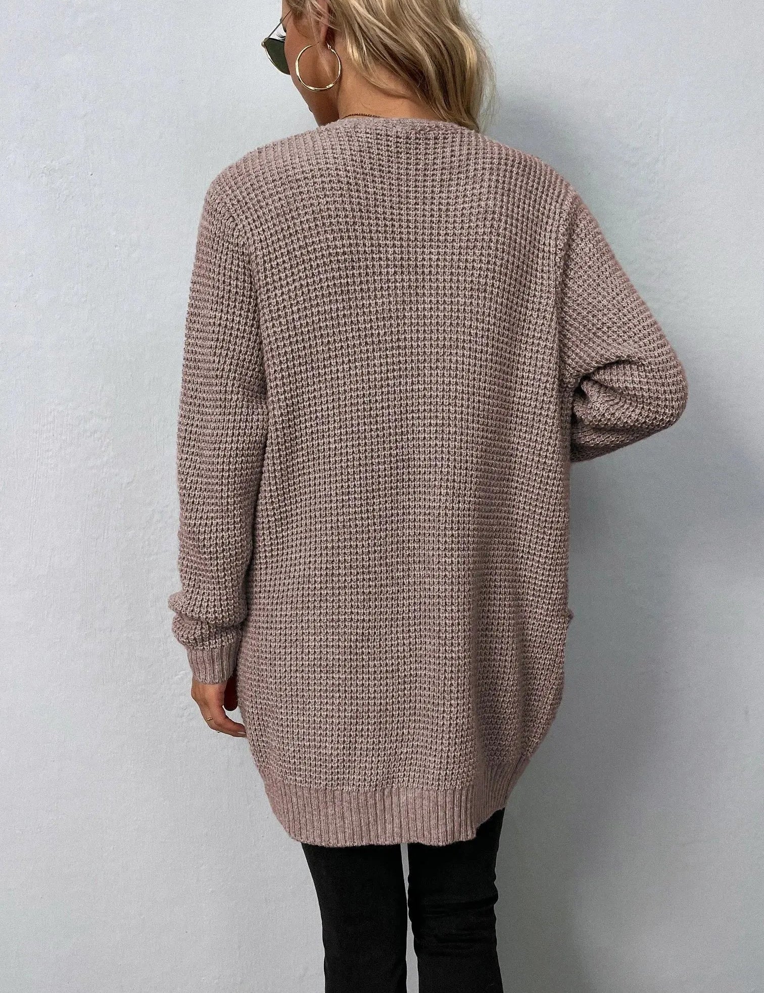 Donna con cardigan lungo beige, lavorato a maglia, indossa occhiali da sole e orecchini a cerchio. Moda autunnale casual, stile confortevole.