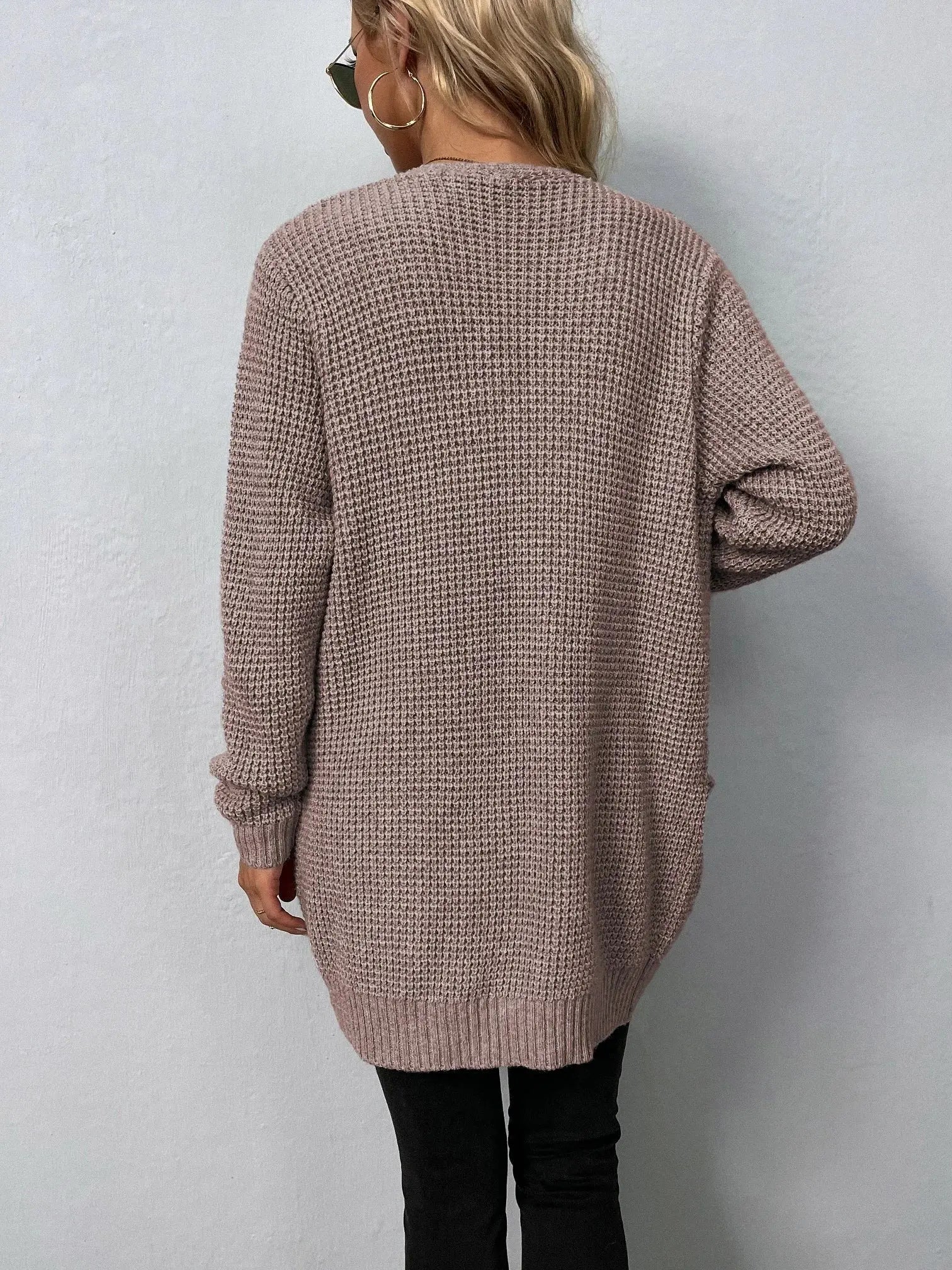 Donna con cardigan lungo beige, lavorato a maglia, indossa occhiali da sole e orecchini a cerchio. Moda autunnale casual, stile confortevole.