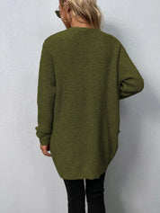 Donna con maglione verde oliva a maglia grossa, maniche lunghe, indossa occhiali da sole e orecchini a cerchio, sfondo bianco. Moda autunnale casual.