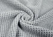 Tessuto a nido d'ape grigio chiaro, texture morbida e accogliente, ideale per coperte e abbigliamento invernale. Materiale caldo e traspirante.