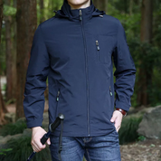Giacca impermeabile blu scuro da uomo, con cappuccio e zip, indossata in ambiente boschivo. Ideale per escursioni e attività outdoor.
