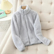 Giacca in pile grigio chiaro su divano beige, design con zip, morbida e calda, ideale per l'inverno. Abbigliamento casual, moda donna.
