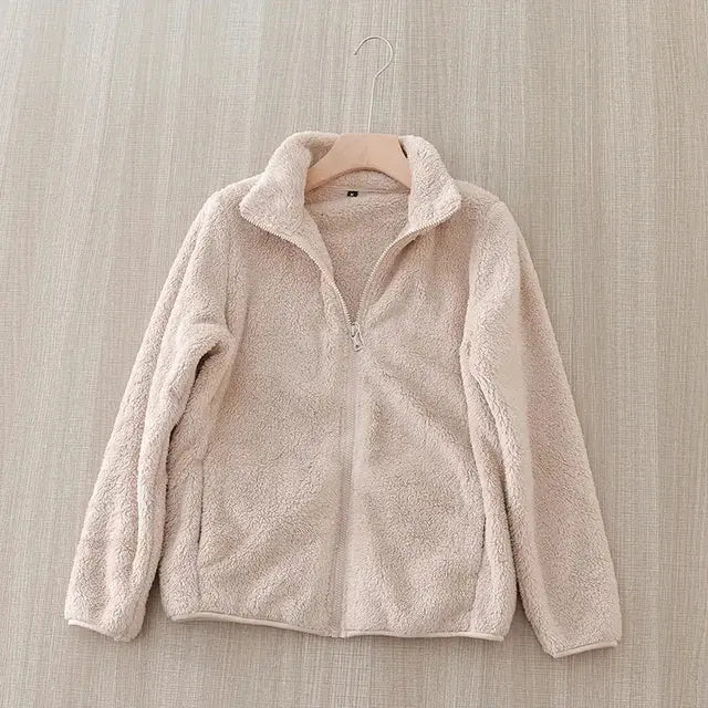 Giacca in pile beige appesa su gruccia, tessuto morbido e caldo, ideale per l'inverno. Design casual, chiusura con zip, perfetta per look quotidiani.