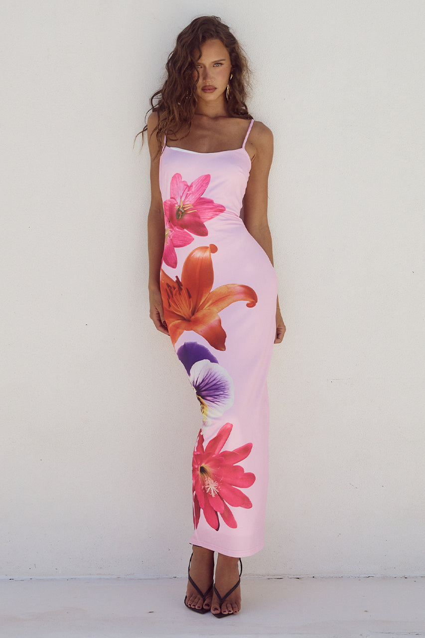 Abito lungo estivo rosa con stampa floreale vivace, spalline sottili, indossato da modella su sfondo bianco. Moda donna, abbigliamento elegante.