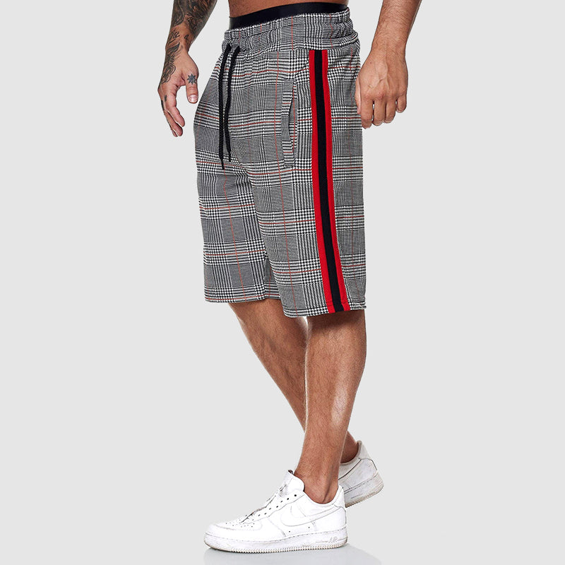 Shorts uomo a quadri grigi con strisce rosse e nere, elastico in vita, cordoncino nero, indossati con scarpe da ginnastica bianche.