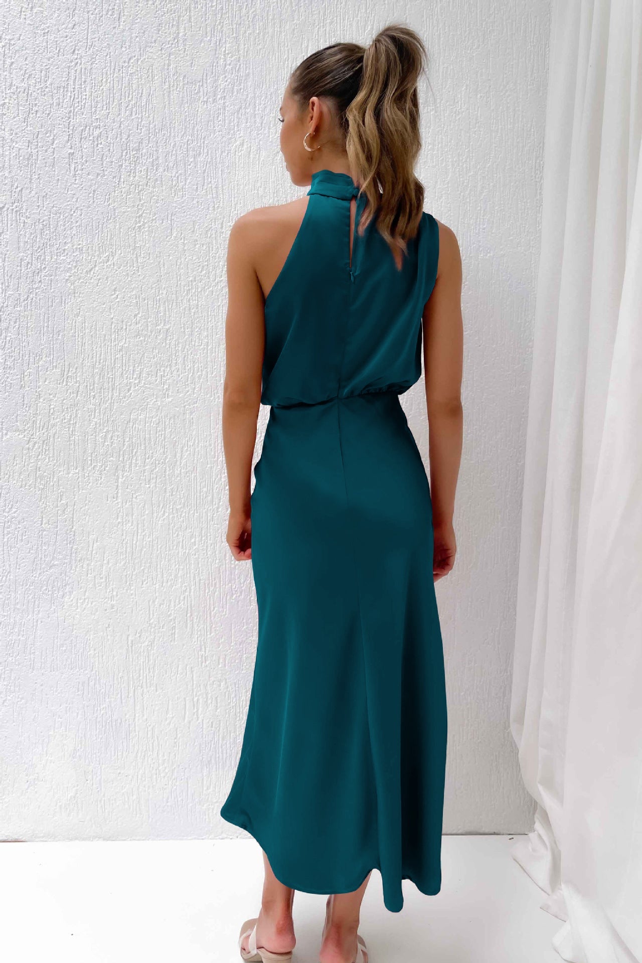 Donna in abito lungo verde smeraldo, senza maniche, con collo alto. Moda elegante, abbigliamento estivo, abito da sera femminile.