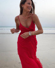 Donna sorridente in abito rosso su spiaggia al tramonto, mare sullo sfondo. Moda estiva, abbigliamento elegante, vacanza al mare.
