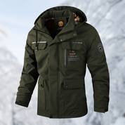 Giacca invernale verde con cappuccio, tasche multiple e dettagli riflettenti, ideale per escursioni in montagna. Tessuto resistente e impermeabile.