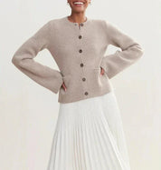Cardigan beige in lana con bottoni marroni, abbinato a gonna plissettata bianca. Moda donna elegante, abbigliamento autunnale chic.