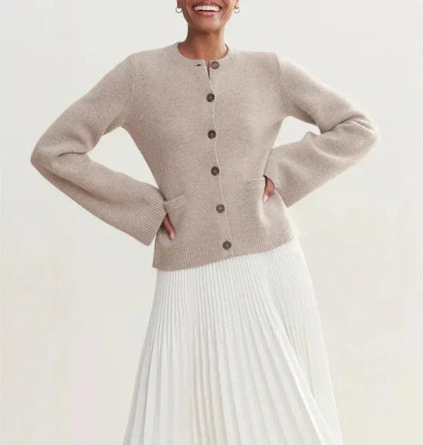 Cardigan beige in lana con bottoni marroni, abbinato a gonna plissettata bianca. Moda donna elegante, abbigliamento autunnale chic.