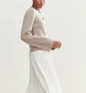 Giacca beige in lana con bottoni, indossata su gonna bianca plissettata. Moda donna elegante, abbigliamento autunnale chic.