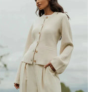 Donna con cardigan beige in lana, abbottonato, maniche lunghe, abbinato a pantaloni coordinati. Moda autunnale elegante e minimalista.