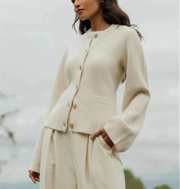 Donna con cardigan beige in lana, abbottonato, maniche lunghe, abbinato a pantaloni coordinati. Moda autunnale elegante e minimalista.
