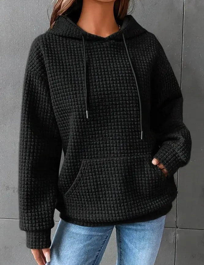 Felpa nera con cappuccio e tasca frontale, tessuto a trama waffle, indossata da una persona. Abbigliamento casual donna, moda autunno inverno.