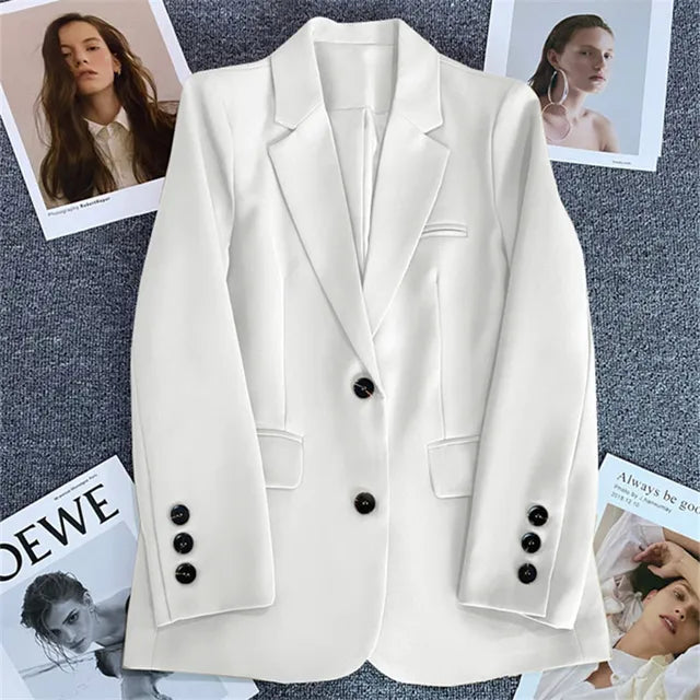 Giacca bianca elegante da donna con bottoni neri su sfondo grigio, circondata da riviste di moda. Stile moderno, ideale per look professionali.