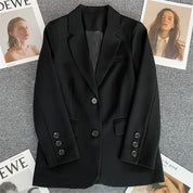 Giacca nera elegante da donna su sfondo grigio, con riviste di moda. Blazer classico, bottoni decorativi, ideale per look formali e casual.