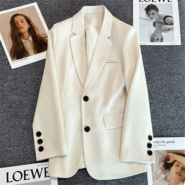 Giacca bianca elegante da donna su sfondo grigio, con bottoni neri e tasche, circondata da riviste di moda. Stile moderno e sofisticato.