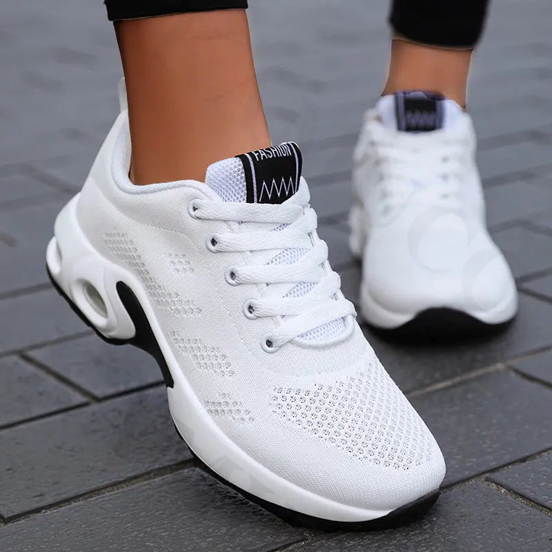 Scarpe da ginnastica bianche unisex, suola ammortizzata, design traspirante, ideali per corsa e sport, su pavimento in pietra grigia.
