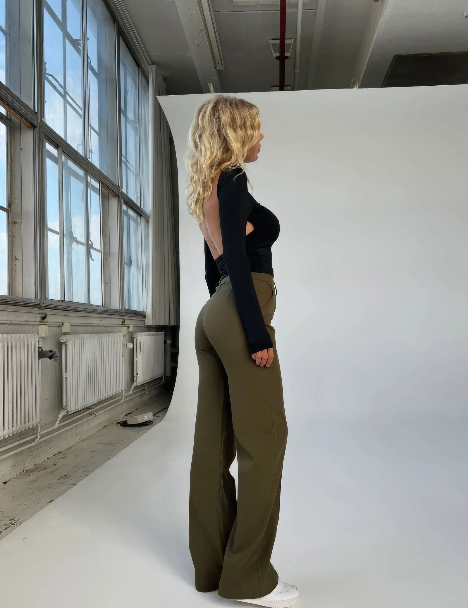 Donna in studio fotografico indossa top nero a maniche lunghe e pantaloni verdi larghi, scarpe bianche. Moda casual, abbigliamento femminile moderno.