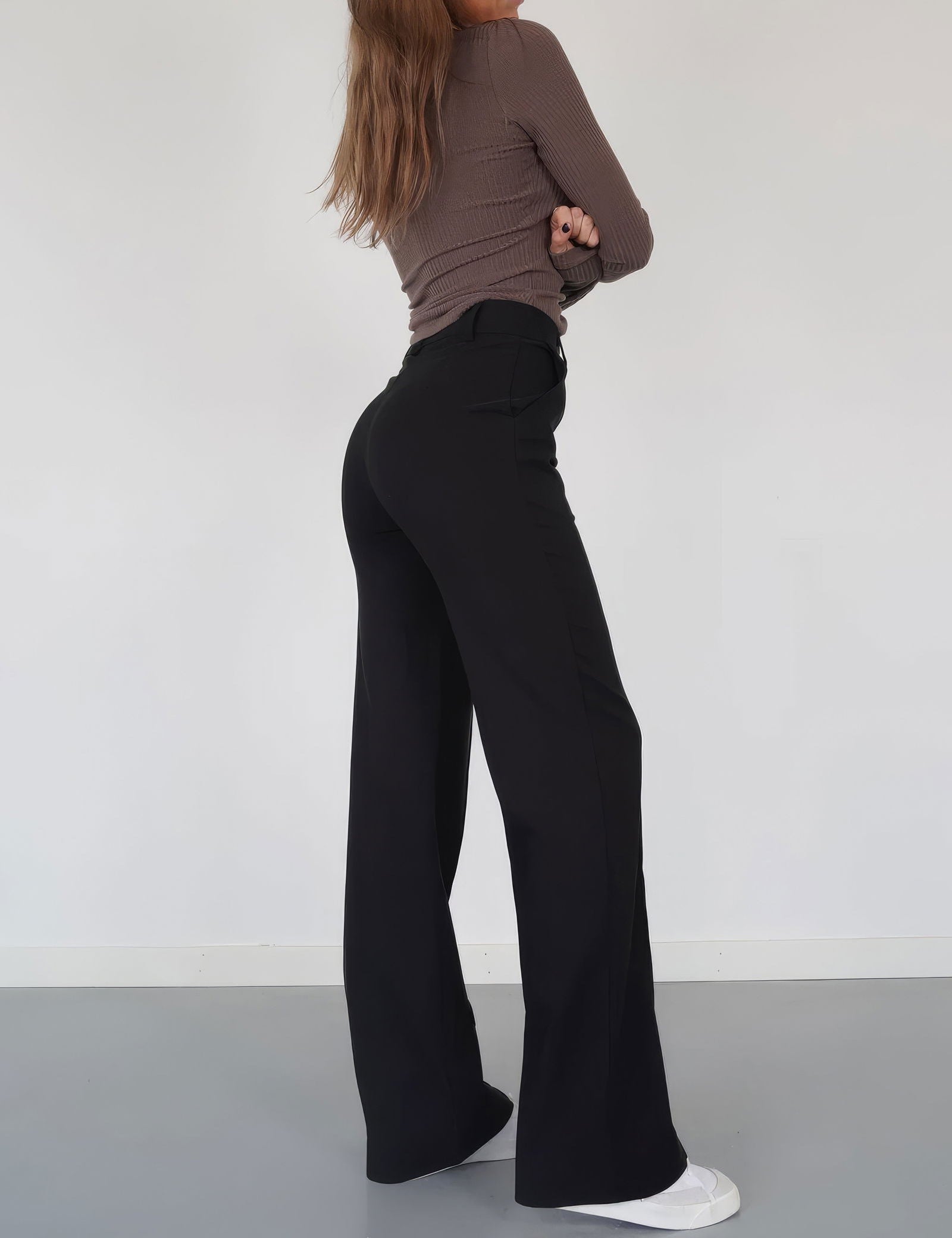 Donna in pantaloni neri a vita alta, maglia marrone a maniche lunghe, scarpe bianche; moda casual elegante, abbigliamento femminile autunnale.