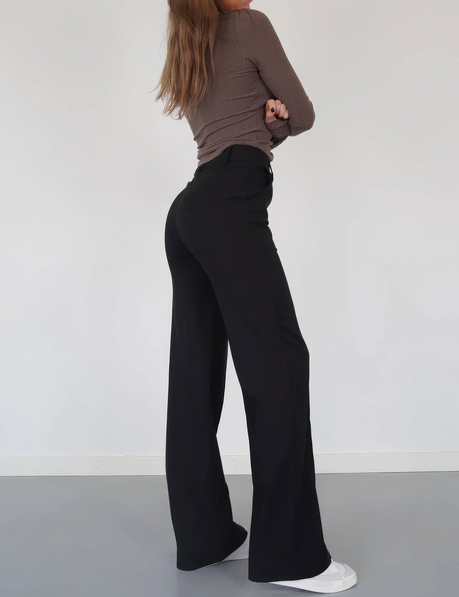 Donna in pantaloni a zampa neri, maglia marrone a maniche lunghe, scarpe bianche. Moda femminile, abbigliamento casual elegante, tendenze 2023.