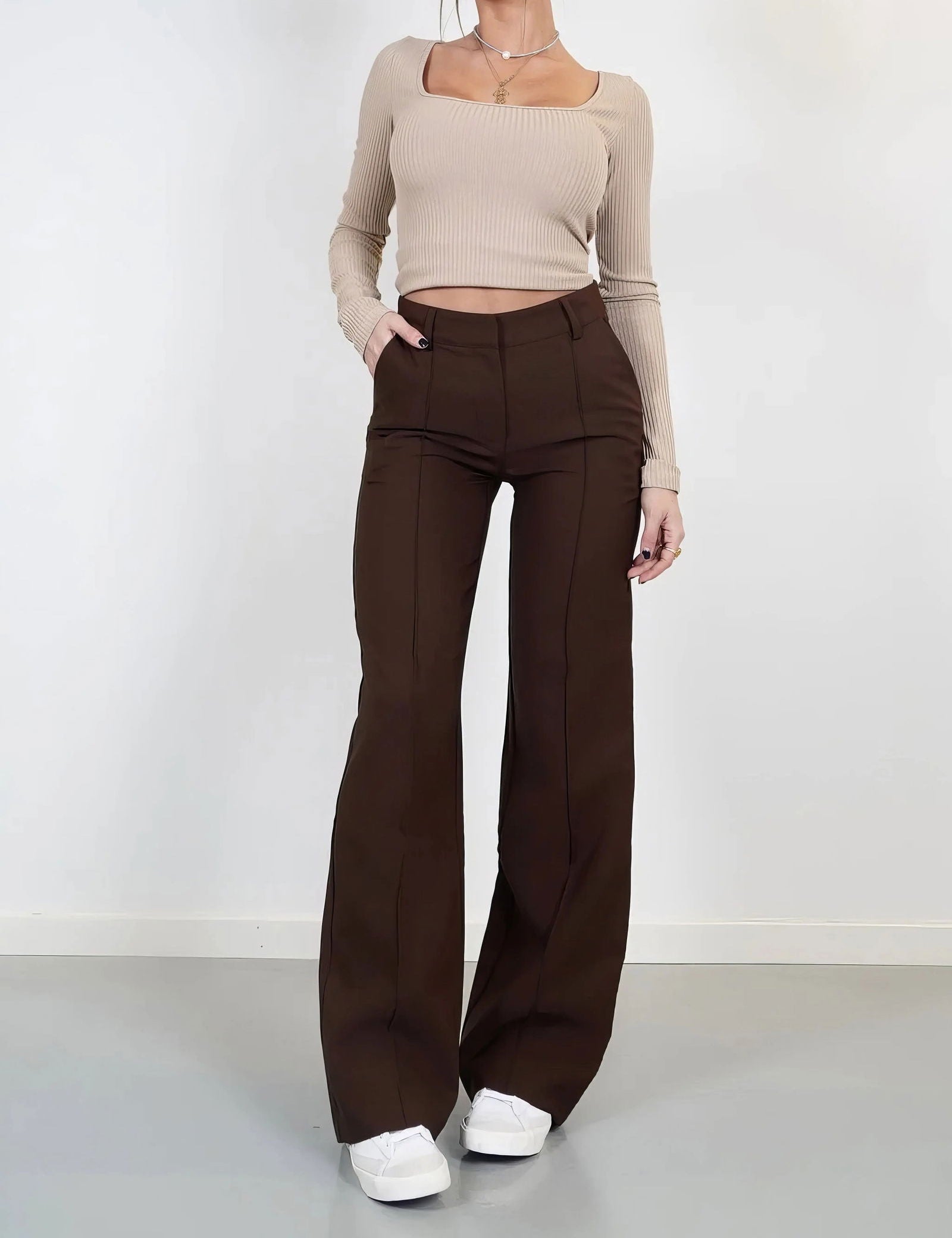 Donna in pantaloni a zampa marroni e top beige a coste, scarpe bianche. Moda casual elegante, abbigliamento autunnale, tendenze 2023.