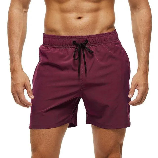Uomo in pantaloncini da bagno bordeaux, elastico in vita con laccio nero, tessuto leggero, ideale per nuoto e sport estivi.