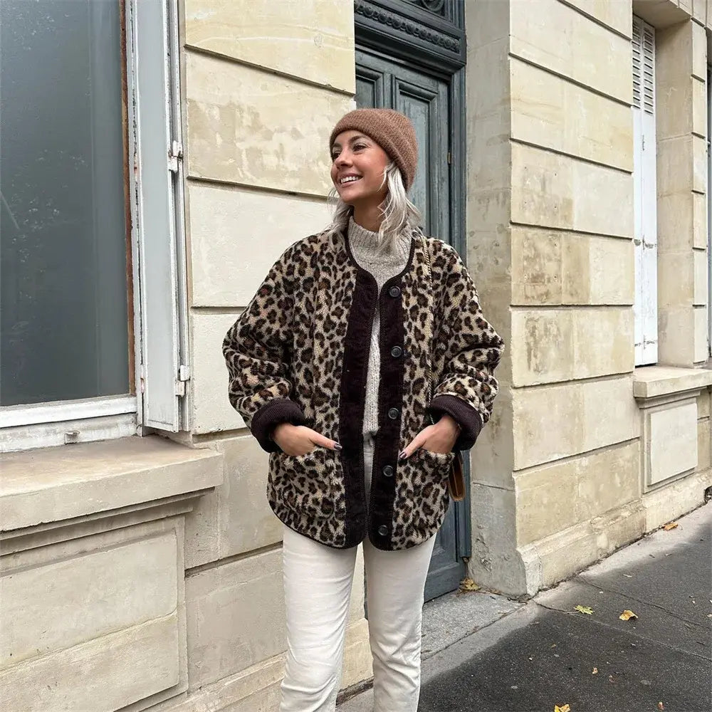 Giacca in pelliccia sintetica leopardata, donna sorridente, cappello marrone, maglione grigio, pantaloni bianchi, moda autunnale urbana.