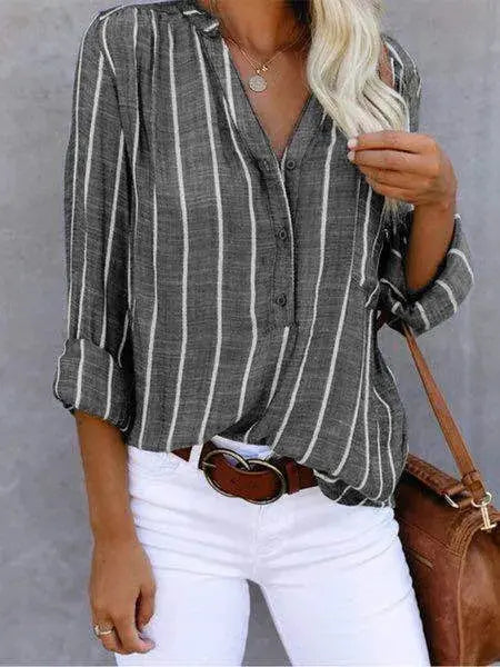 Camicia a righe verticali grigie e bianche, maniche lunghe, abbinata a pantaloni bianchi e borsa marrone. Moda casual donna, stile elegante.