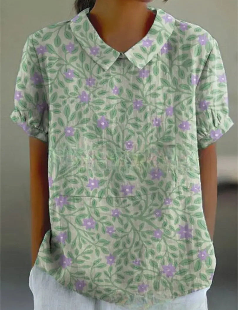 Camicia donna estiva a maniche corte con stampa floreale verde e viola, colletto classico, tessuto leggero, ideale per look casual e freschi.