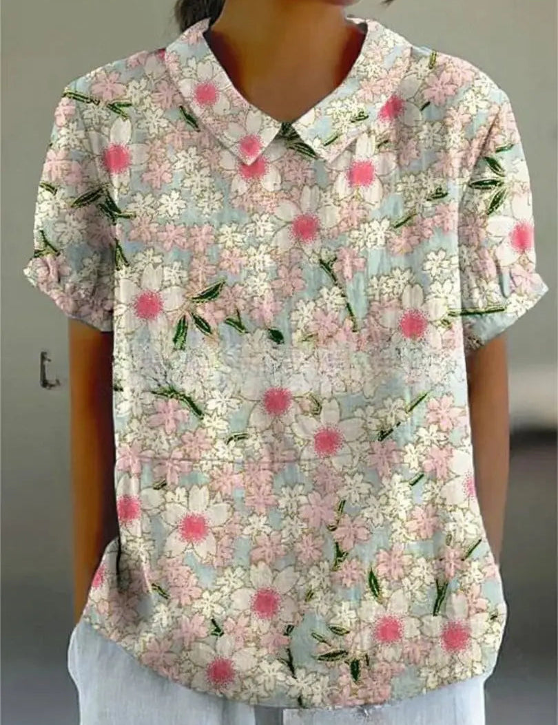 Camicia donna a maniche corte con colletto, fantasia floreale rosa e bianca su sfondo azzurro. Stile casual estivo, tessuto leggero e traspirante.