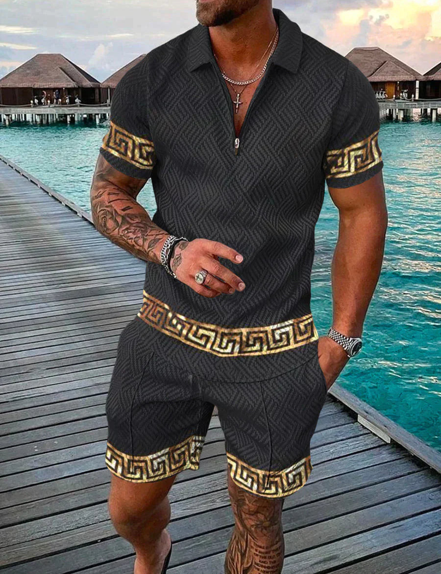 Uomo in completo estivo nero con motivi dorati, camicia a polo e pantaloncini coordinati, su passerella di legno vicino al mare. Moda estiva elegante.