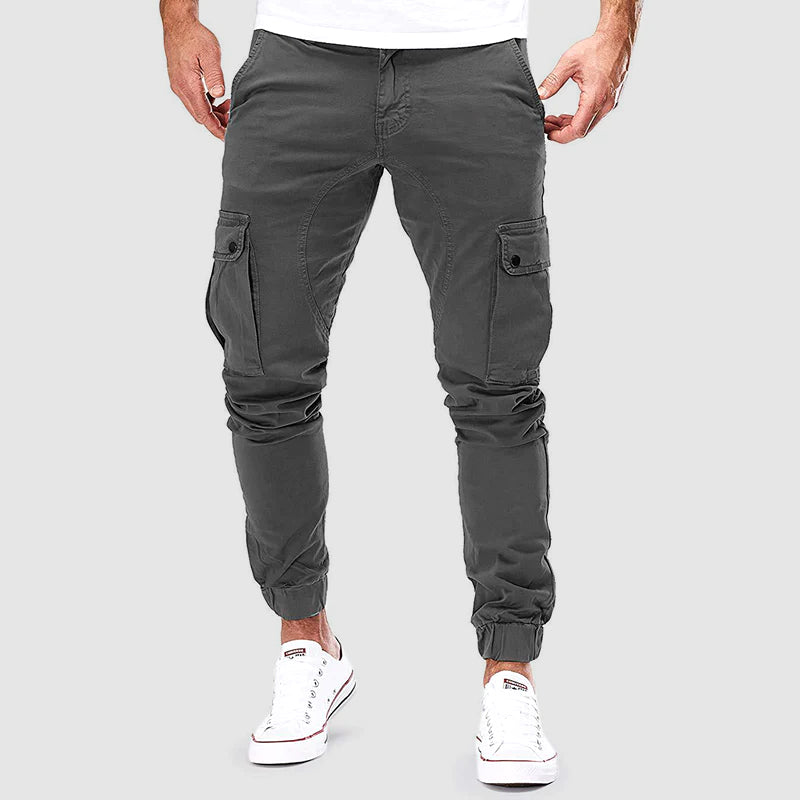 Pantaloni cargo uomo grigi, tasche laterali, vestibilità slim, stile casual, perfetti per moda urbana. Indossati con sneakers bianche.