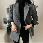 Giacca donna elegante grigia, stile casual chic, abbinata a maglione nero. Moda autunnale, outfit versatile per ufficio o eventi formali.